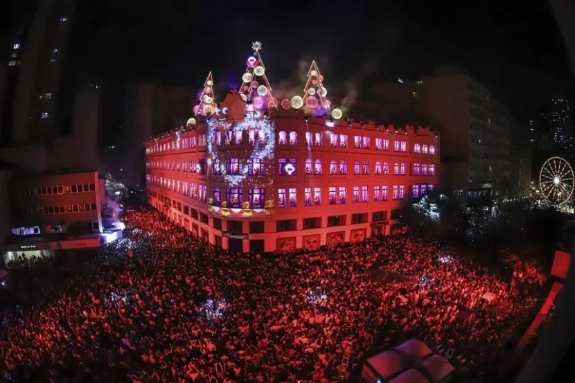 Palácio Avenida anuncia datas do Coral de Natal: cinco apresentações confirmadas Palácio Avenida anuncia datas do Coral de Natal: cinco apresentações confirmadas Subtítulo: Espetáculo gratuito terá ensaio geral em 5 de dezembro; apresentações ocorrem em dois finais de semana para celebrar o Natal em Curitiba ⸻ O Coral de Natal do Palácio Avenida, uma das atrações mais emblemáticas do fim de ano em Curitiba, já tem datas definidas para 2025. Foi confirmado que o ensaio geral acontecerá na sexta-feira, dia 5 de dezembro, marcando oficialmente o início dos preparativos para as apresentações ao público.  As apresentações acontecem em cinco datas distintas: 6, 7, 12, 13 e 14 de dezembro, sempre às 20h15. Três desses dias caem em finais de semana, facilitando o acesso de moradores e visitantes que desejam vivenciar a atmosfera natalina no centro da cidade.  O anúncio foi feito pelo prefeito de Curitiba, Eduardo Pimentel, nas redes sociais. Ele ressaltou que faltam cerca de cem dias para marcar “o maior Natal do país” e convidou as famílias para participarem de um dos eventos mais tradicionais da cidade.  O Coral de Natal do Palácio Avenida se tornou, ao longo dos anos, uma tradição querida por muitos curitibanos. A apresentação em si mistura canto coral, projeções luminosas sobre a fachada do prédio histórico, música natalina e efeitos visuais que visam emocionar. O espetáculo é gratuito, o que reforça seu papel de celebração comunitária e cultural. (Nota: detalhes exatos do repertório não foram divulgados até o momento.) Para quem quiser assistir, é bom ficar atento: por tratar-se de evento de grande porte, frequentemente há grande demanda pelo local e horários. Vale a pena planejar com antecedência, chegando cedo para garantir bom lugar, especialmente nos finais de semana. Também é provável que sejam tomadas medidas de segurança e controle de público, como em anos anteriores. Curitiba, com essa programação cultural natalina, reforça seu apelo turístico e comunitário nessa época do ano. O Coral de Natal do Palácio Avenida promete ser novamente um ponto de encontro de emoções, luzes e esperança — elementos que se somam ao espírito natalino, proporcionando momentos memoráveis para pessoas de todas as idades.